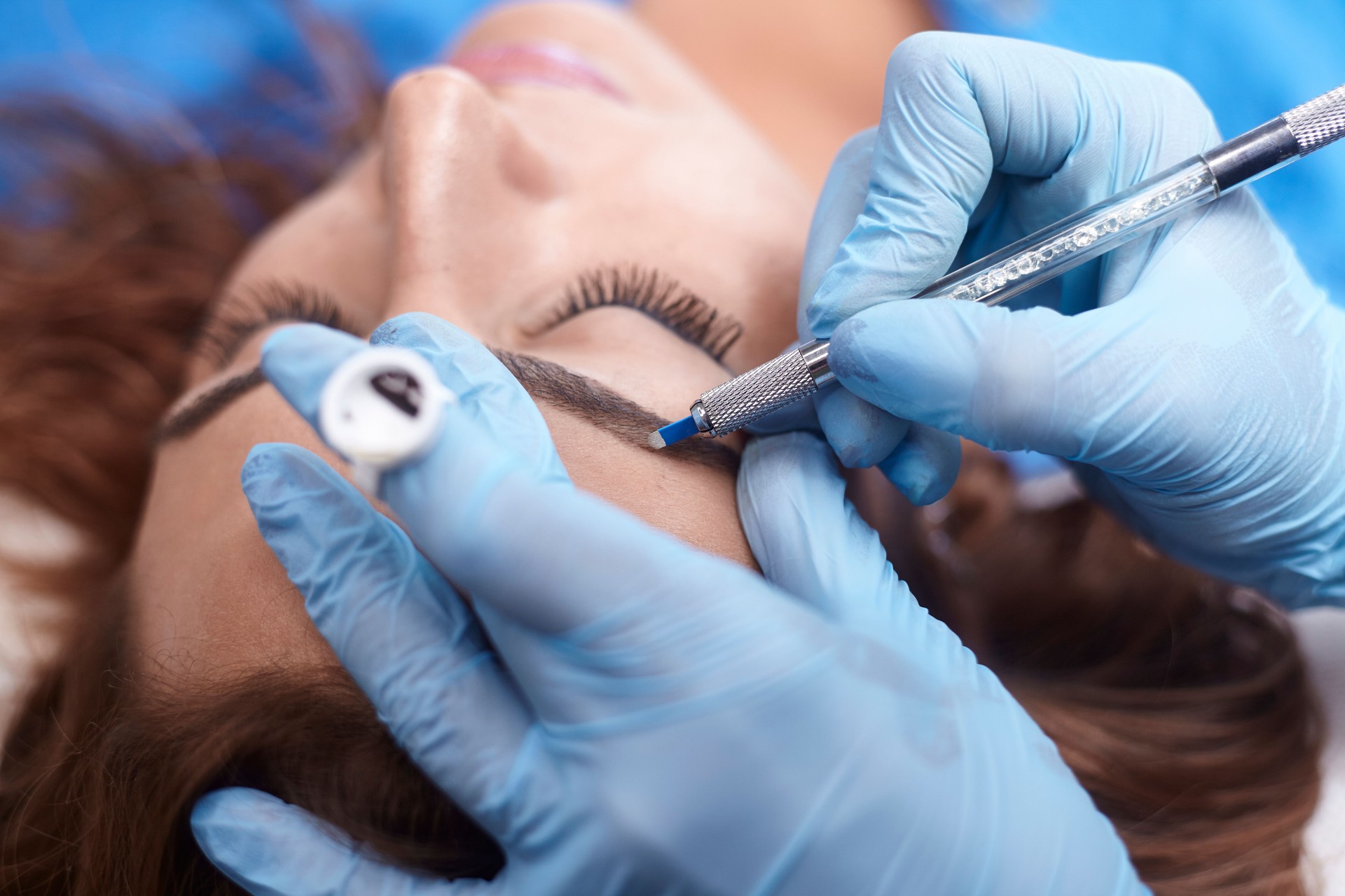 microblading close-up, hands adding pigment to eyebrows.